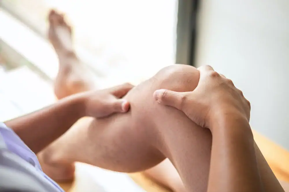 A person sitting and holding their knee with both hands, appearing to massage or check it, possibly indicating pain or discomfort&mdash;an image often seen in Physical & Occupational Therapy across Suffolk & Nassau County, NY.