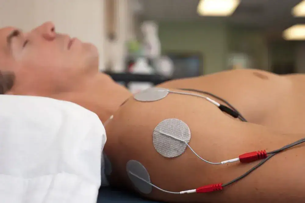 Person undergoing electrotherapy with electrodes on shoulder.