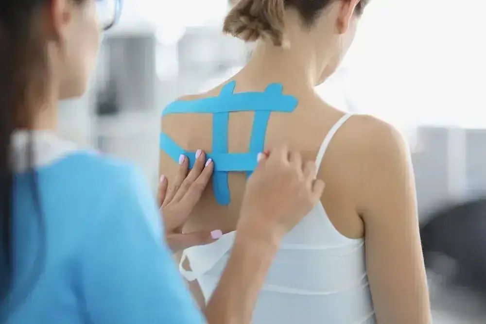 Therapist applying blue kinesiology tape on woman's back in clinic.