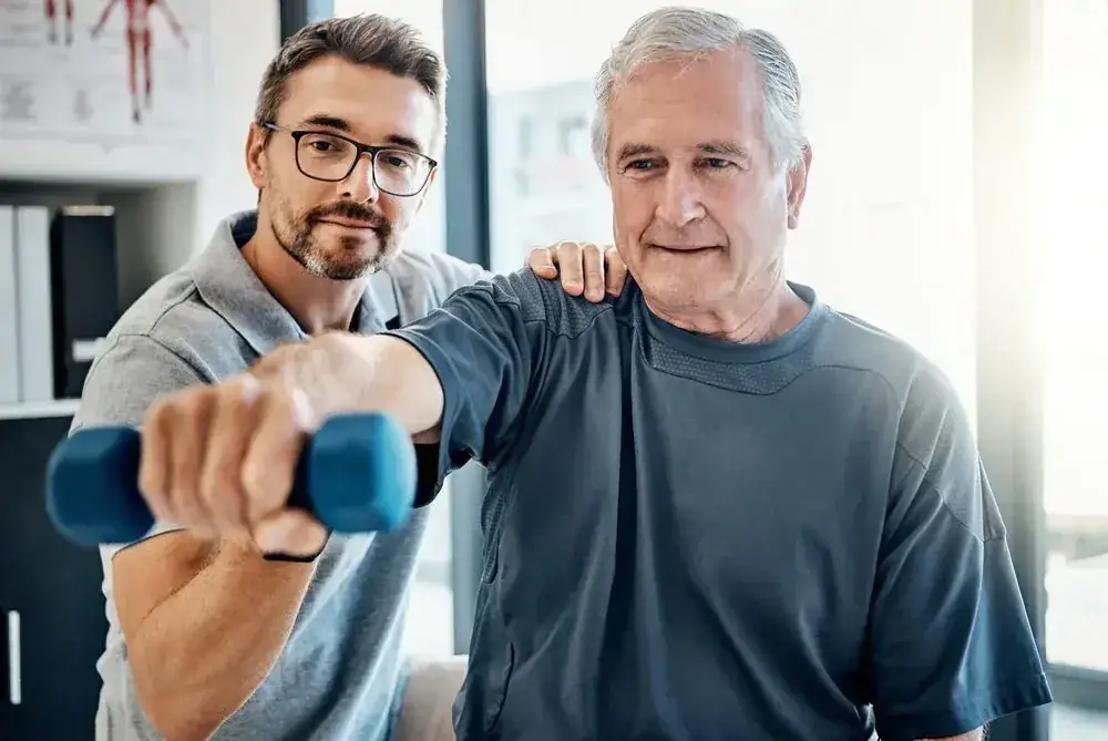 Senior man exercising with dumbbell guided by a therapist.