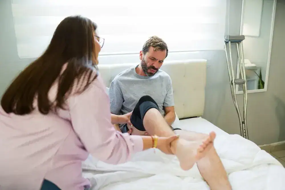Physiotherapist helping a man with knee rehabilitation on a bed.