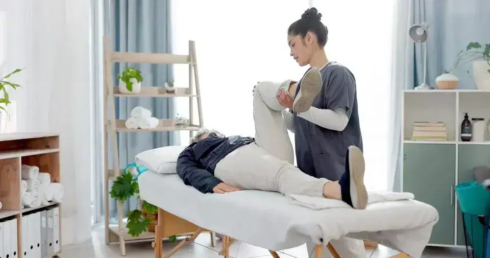Physiotherapist aiding a patient with leg exercise on a table.